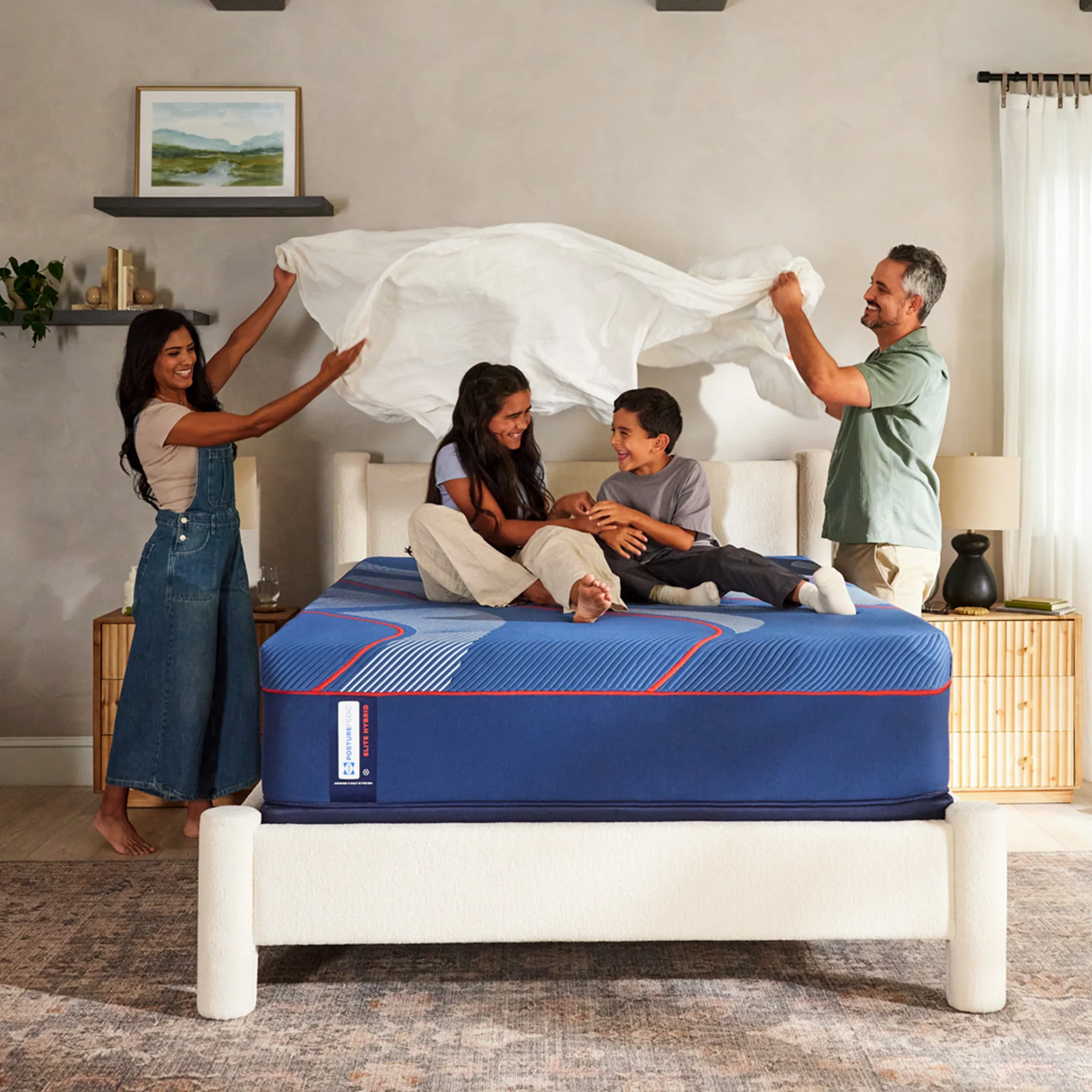 Sealy Brenham Soft Hybrid Mattress 1 Family enjoying the Sealy Brenham Soft Hybrid Mattress, featuring a blue and red design, with a woman and man playfully adjusting bedding while two children sit on the mattress.