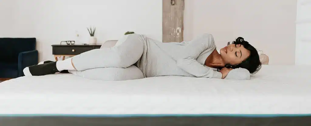 Woman comfortably lying on a mattress, promoting better sleep and relaxation, in a cozy bedroom setting with modern decor.